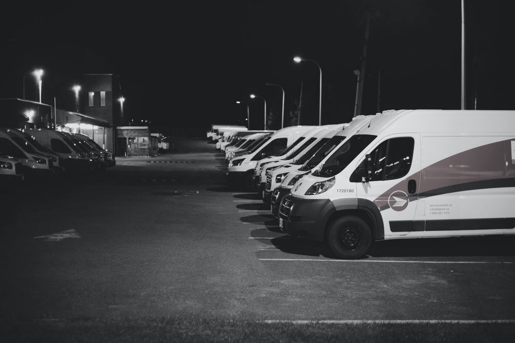 A cold-chain courier fleet staged under lights before a night dispatch.
